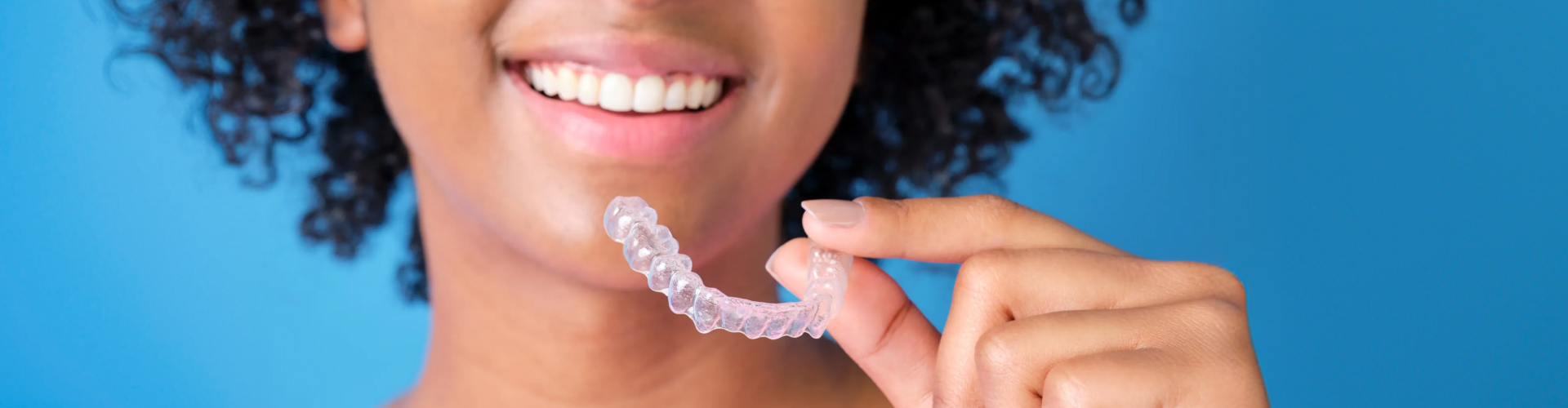 Smiling patient holding a clear Invisalign aligner near their teeth.